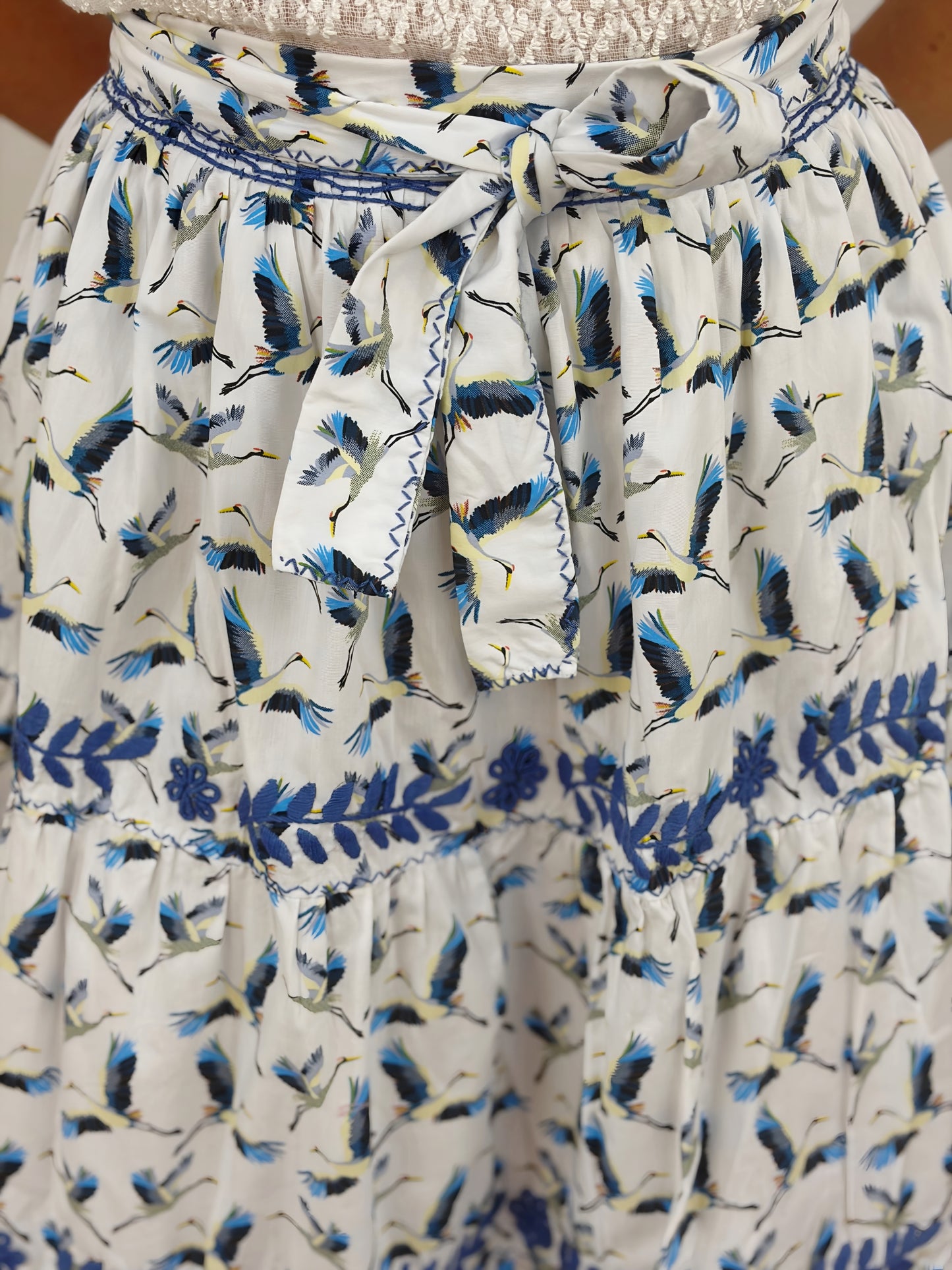 Falda vuelos Aguacatenango color blanco estampado de garzas, bordado azul, detalle del bordado y cinta. 