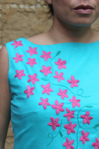 Vestido acampanado, bordado de flores, color turquesa, bordado fucsia, detalle del bordado.